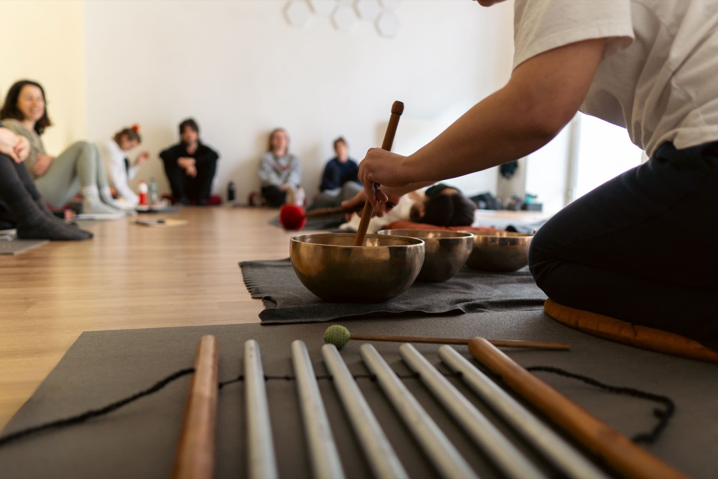 Hände spielen eine Klangschale, im Vordergrund Klangstäbe während einer Sound-Healing-Ausbildung