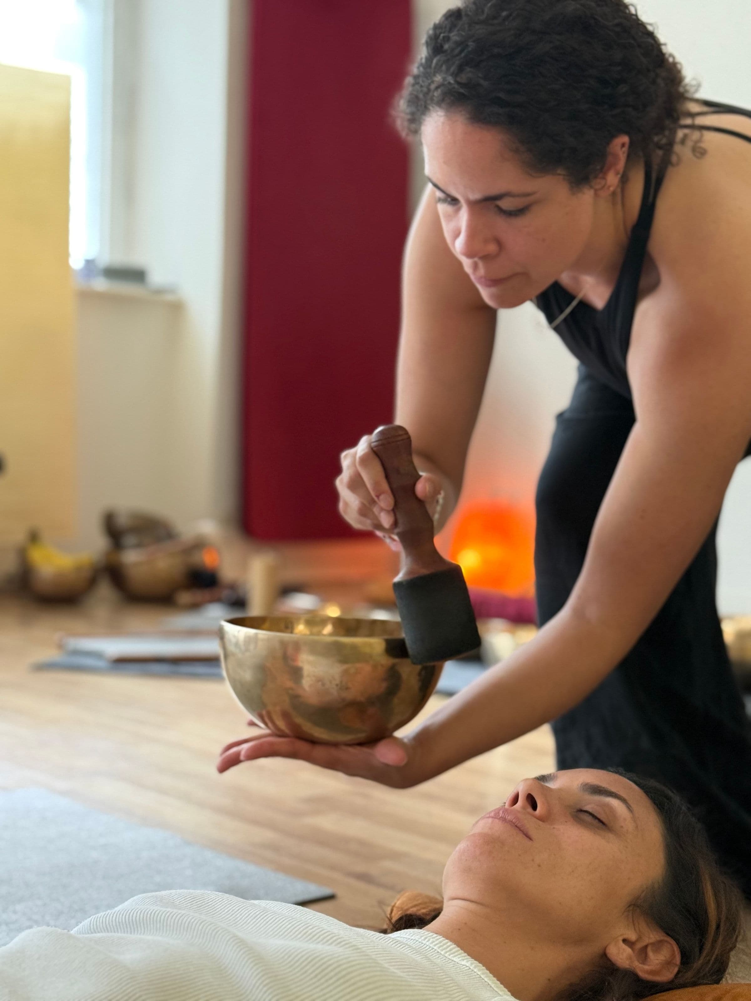 A participant holds a singing bowl beside another participant lying on a mat during sound healing practice at the Yogicescape studio.