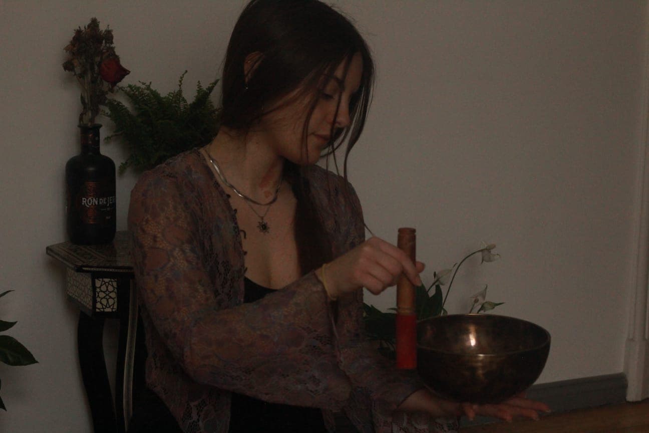 Myrto Kanellopoulou spielt eine Klangschale mit Holzklöppel in gedämpftem, warmem Licht