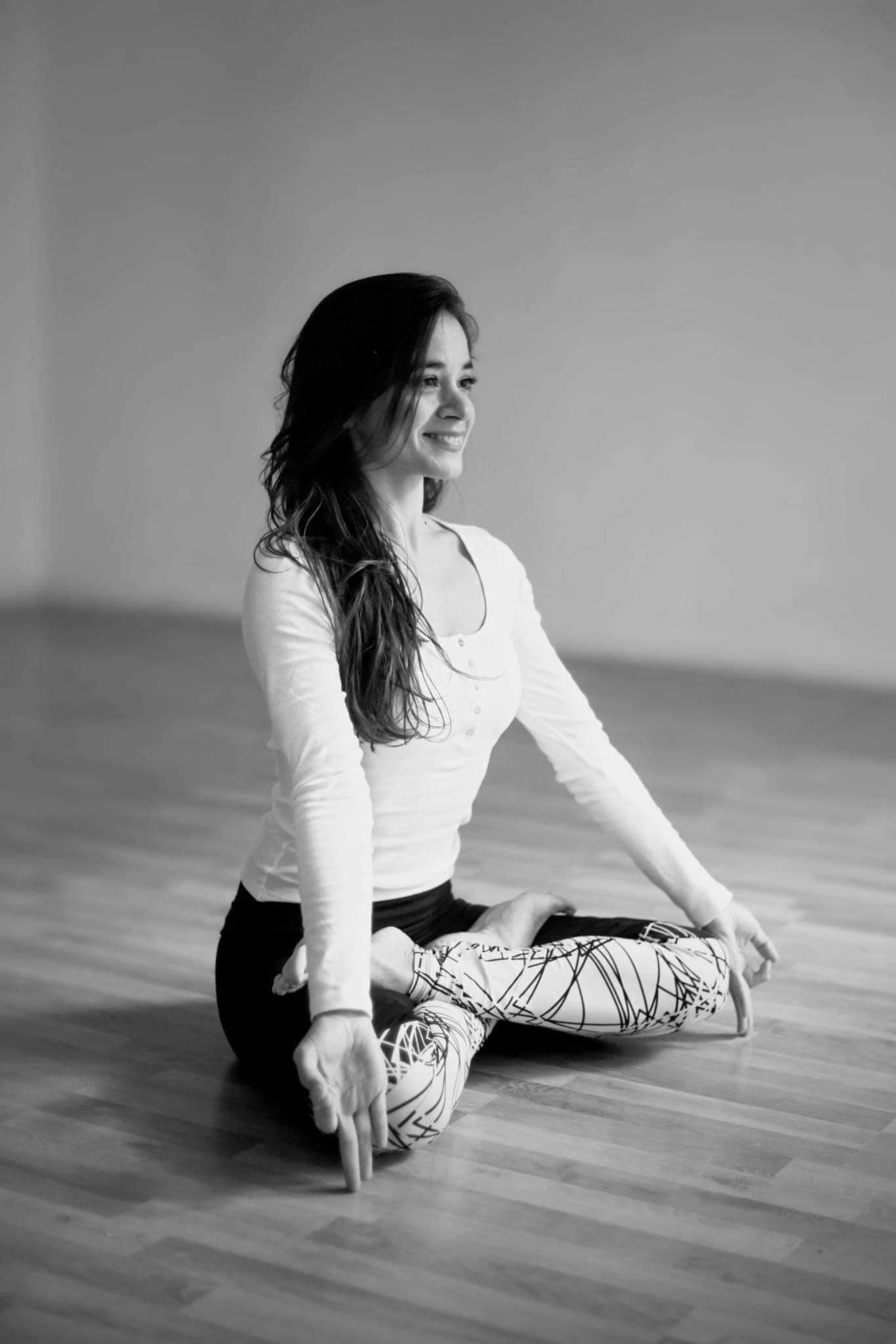 Nadine Kopprio seated cross-legged on a wooden floor, smiling, black-and-white photograph