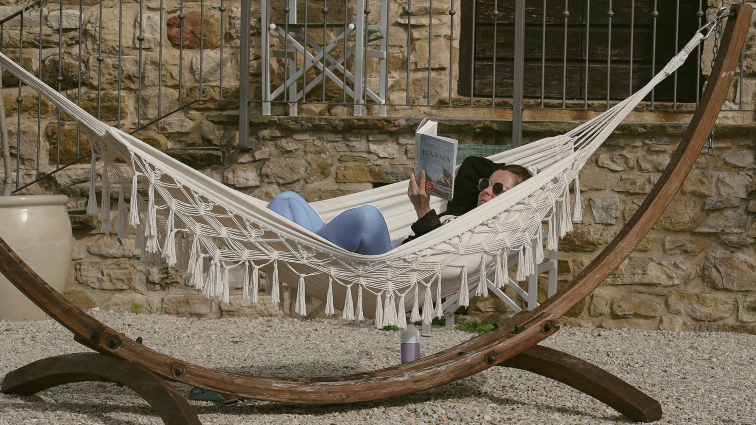 A guest reads a book in a hammock in the courtyard of a stone farmhouse