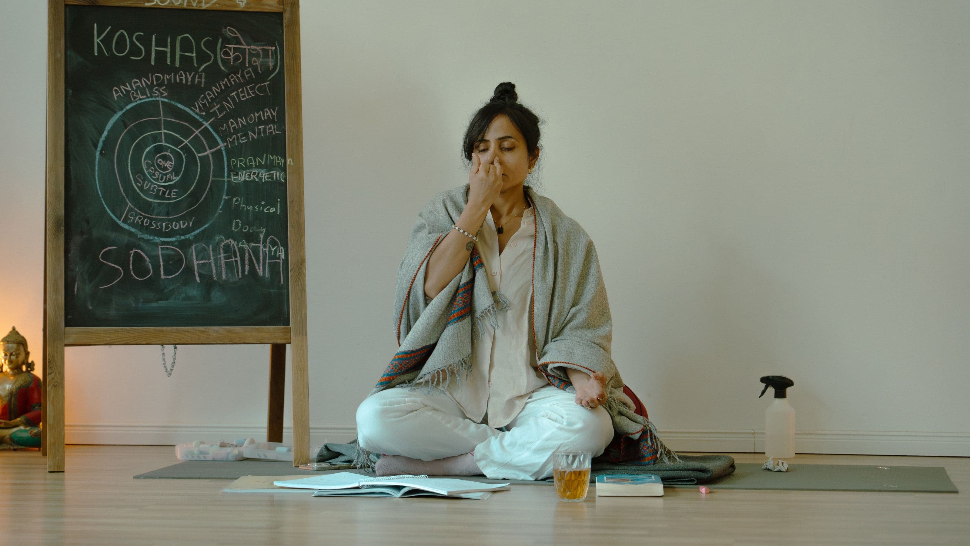 Neha Pugalia zeigt die Wechselatmung neben einer Tafel beim Pranayama-Präsenztraining im Yogicescape-Studio