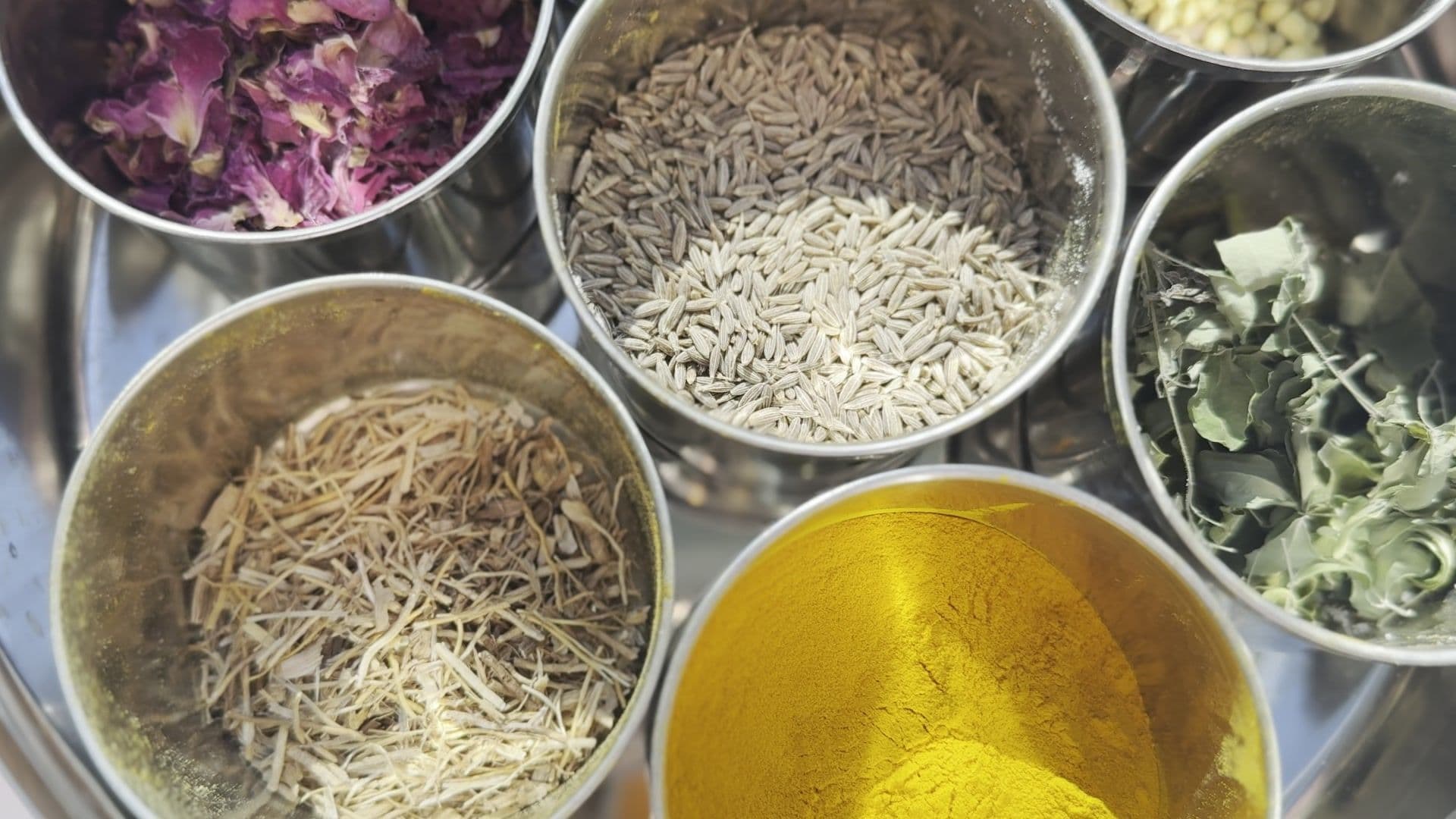 Ayurvedic herbs and spices — turmeric, cumin, rose petals and dried herbs — laid out at a Yogicescape Ayurveda training in Berlin